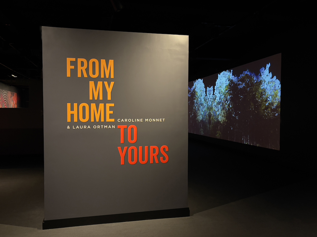 The entrance to the gallery where the film "From My Home to Yours" is projected in the background. 